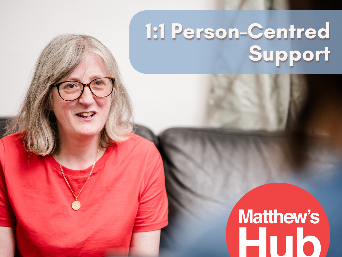 1:1 Person Centred Support. A woman in a red t-shirt and glasses talks to a woman in blue