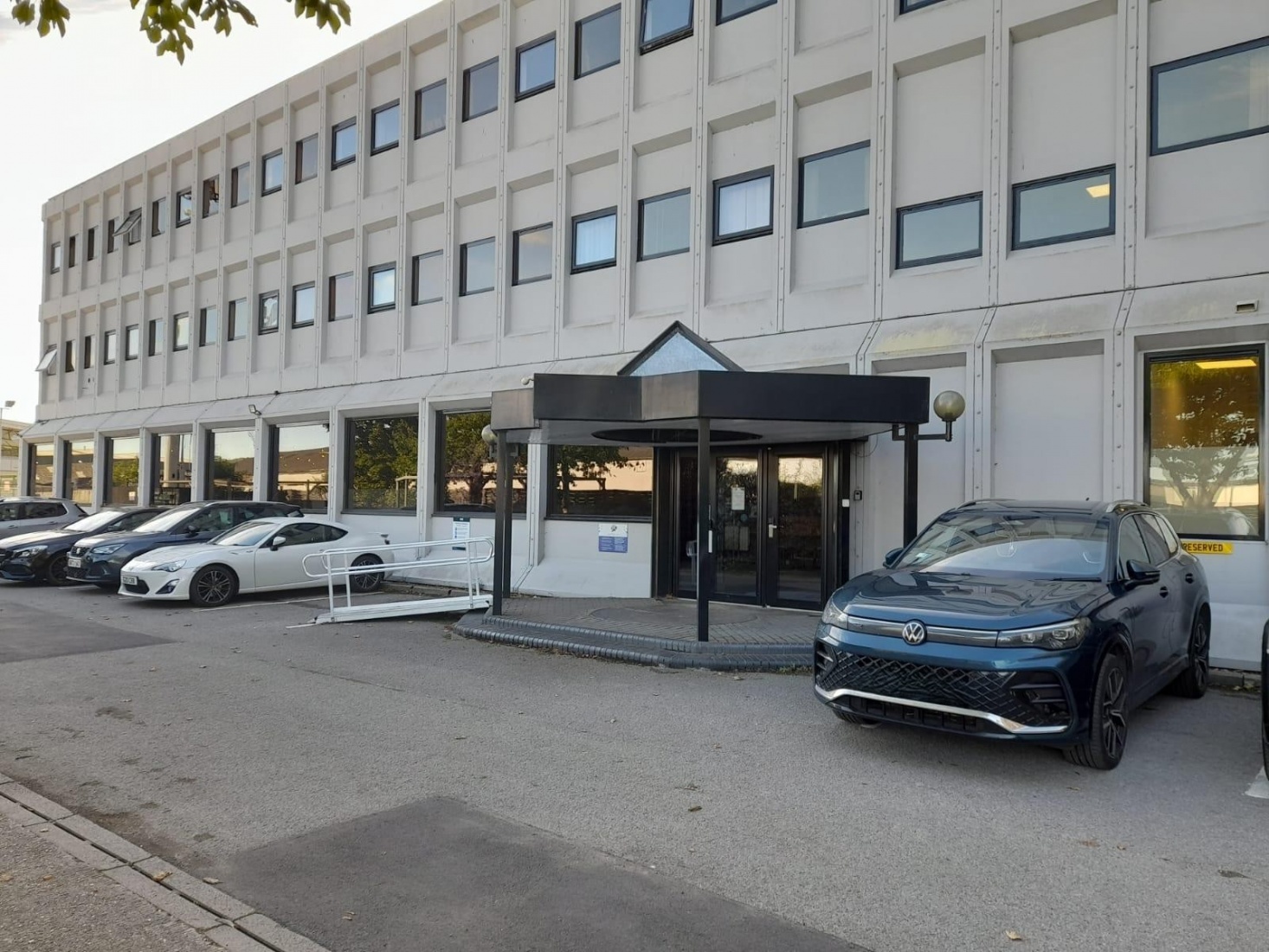 A building entrance way with cars parked in front and a silver ramp.