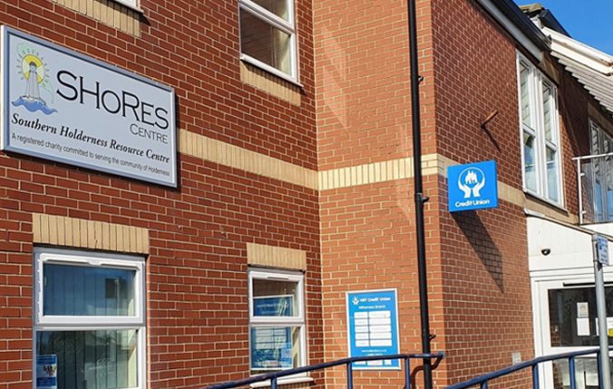 A brick building with white windows and doors and a large sign which says SHORES South Holderness Resource Centre