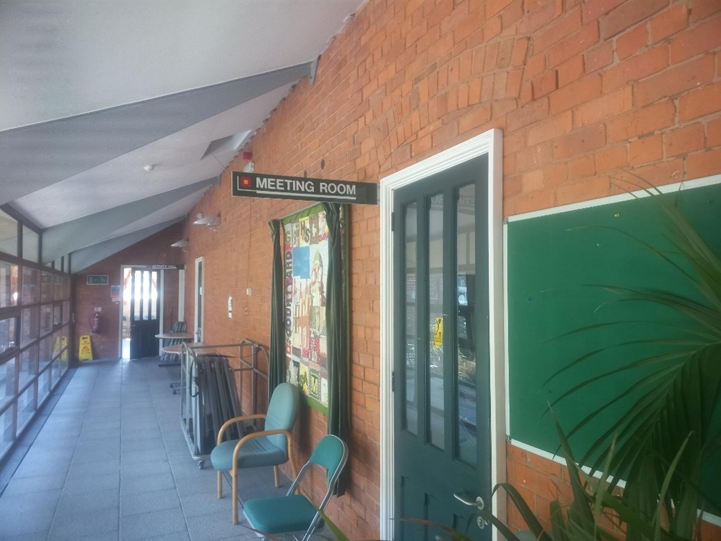 The corridor showing the entrance to the meeting room, there is a sign above the door.
