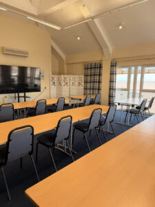 A room with chairs and tables set out in a classroom style with a TV at the front